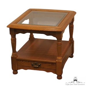 May include: A wooden end table with a glass top and a drawer. The table has turned legs and a simple design.