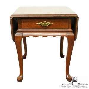 May include: A brown wooden end table with a single drawer and cabriole legs. The table has a drop leaf on each side.