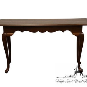 May include: A dark brown wooden console table with a scalloped apron and curved legs. The table has a rectangular top and is designed in a classic style. The legs are gracefully curved, adding to its elegant appearance.