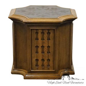 May include: A wooden octagonal end table with a carved design on the front and a dark brown top. The table has a scalloped base.