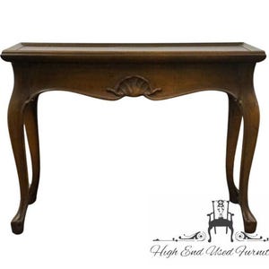 May include: A dark brown, antique-style console table with a rectangular top and curved legs. The table features a decorative shell-shaped carving on the apron. The table is made of wood and has a glossy finish.