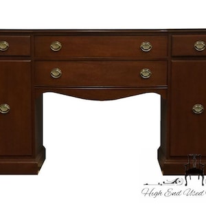 May include: A mahogany wood sideboard with three drawers and two cabinet doors. The sideboard has a curved base and brass hardware.