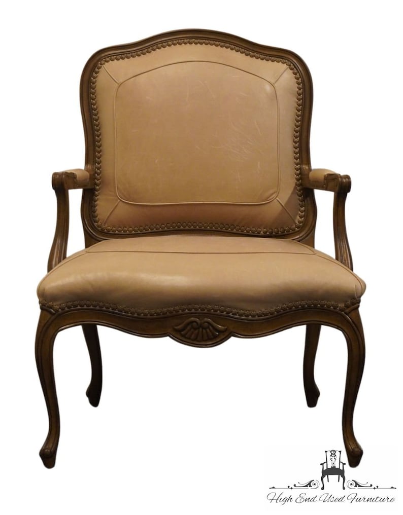 Puede incluir: Un sill&oacute;n de cuero beige con un marco de madera tallada y patas ornamentadas. El sill&oacute;n tiene un respaldo alto y brazos, y el asiento est&aacute; tapizado en cuero suave y flexible.