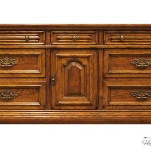 May include: A vintage wooden dresser with six drawers and a cabinet door. The dresser has a rich brown finish and ornate brass hardware.