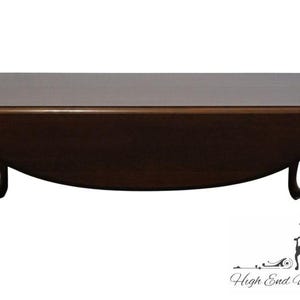 May include: A dark brown, oval-shaped coffee table with a curved apron and four cabriole legs. The table has a smooth, polished surface and is likely made of wood. A classic piece of furniture.