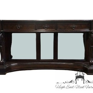 May include: A dark brown wooden console table featuring three drawers with circular metal pulls. The table has a curved base and two ornate, carved legs on each side. The text "High End Used Furniture" is visible in the bottom right corner.
