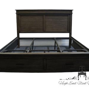 May include: Dark brown wooden bed frame with a headboard and two drawers. The headboard has a rectangular design with horizontal panels. The bed frame has a low profile and a sturdy construction, suitable for a bedroom.