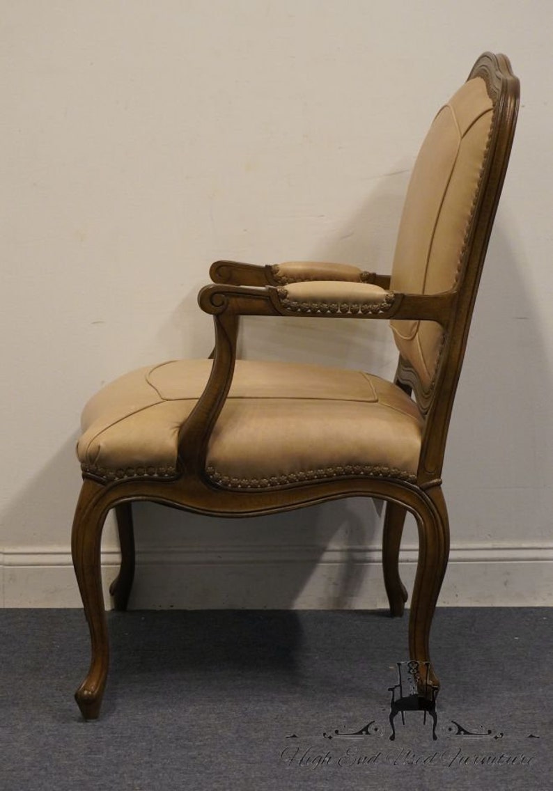 Puede incluir: Vista lateral de una silla de madera marr&oacute;n con un asiento y respaldo tapizados en beige. La silla tiene un dise&ntilde;o tallado en los brazos y las patas. La silla est&aacute; en buen estado y tiene un estilo cl&aacute;sico.