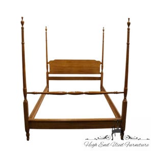 May include: A four-poster bed frame constructed from medium-toned wood. The frame features four tall, slender vertical posts with decorative finials at the top, a rectangular headboard with a curved top edge, and matching side rails.