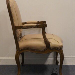 Puede incluir: Vista lateral de un sill&oacute;n tapizado en beige con marco de madera tallada. El sill&oacute;n tiene un respaldo curvo, un asiento acolchado y patas ornamentadas.