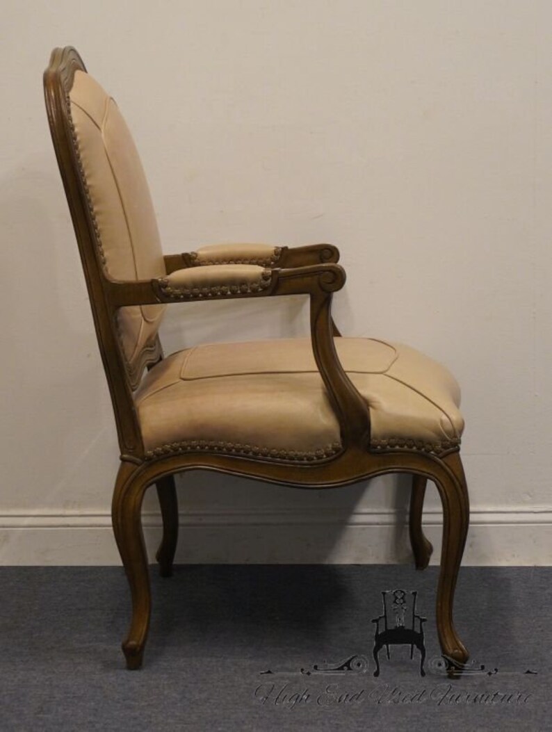 Puede incluir: Vista lateral de un sill&oacute;n tapizado en beige con marco de madera tallada. El sill&oacute;n tiene un respaldo curvo, un asiento acolchado y patas ornamentadas.