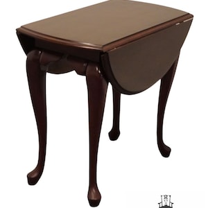 May include: A dark brown, drop-leaf side table with a rectangular top and curved legs. The table has a rich, polished finish and a classic design. The table is approximately 24 inches long, 18 inches wide, and 26 inches high.