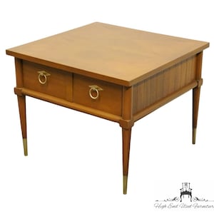 May include: A mid-century modern end table with two drawers and brass hardware. The table has a wood top and legs with brass tips. The table is in good condition and has a warm, honey-brown color.