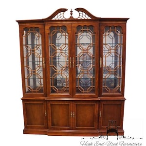 May include: A large, wooden display cabinet with glass doors and geometric lattice detailing. The cabinet has a warm, brown finish and features multiple doors and shelves for storage. The top of the cabinet has an arched design with decorative cutouts. The words "High End Used Furniture" are at the bottom.