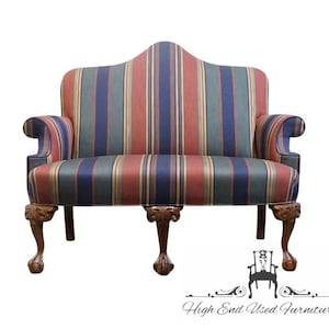 May include: A loveseat upholstered in a multi-colored striped fabric featuring vertical bands of navy blue, muted red, and sage green. The furniture piece has a curved backrest, rolled arms, and three carved wooden legs with ball and claw feet.