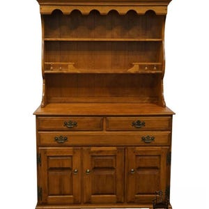 May include: A wooden hutch with a warm, medium-brown finish. It features a top section with shelves and a scalloped edge, and a lower section with drawers and cabinet doors. The hardware is a dark metal. The piece is a classic style.
