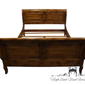 May include: A wooden sleigh bed with a dark brown finish. The headboard and footboard have rectangular panels. The bed frame has curved sides and legs. The bed is designed for a mattress and box spring.