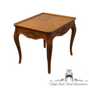 May include: A carved wooden end table with a square top and four legs. The table is made of a light brown wood and has a decorative design on the legs and top.