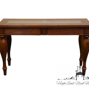 May include: A rectangular wooden desk with a glass top and a drawer. The desk has a dark brown finish and ornate, curved legs. The drawer features a decorative circular design. The desk is a piece of furniture.