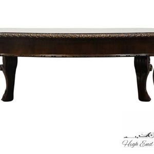 May include: A dark brown oval coffee table with intricate carvings on the legs. The table has a smooth, polished surface and a slightly raised edge.