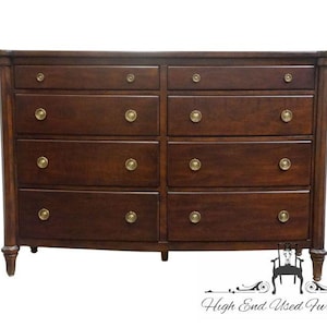 May include: A dark brown wooden dresser featuring ten drawers arranged in two vertical columns. Each drawer is equipped with two circular brass-toned metal knobs. The piece stands on four short, turned legs and has a smooth, polished finish.