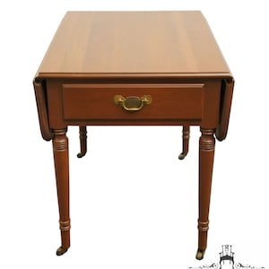 May include: A brown wooden drop leaf table with a single drawer and turned legs. The table has brass hardware and casters.