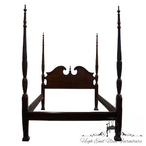 May include: A dark brown four-poster bed frame with a headboard. The bed frame has four tall posts with decorative carvings and finials. The headboard has a curved top. The bed frame is made of wood.