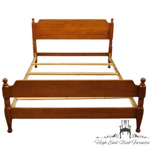 May include: A wooden bed frame with a warm brown finish, featuring a tall headboard and a shorter footboard. Both ends have smooth, arched top rails and rounded finials on the corner posts. The frame includes side rails and wooden slats.