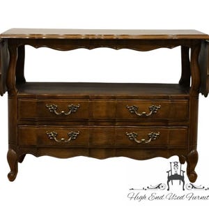 May include: A dark brown wooden console table with two drawers and ornate brass handles. The table has a scalloped edge and curved legs. The top has drop leaves on each side. The table is a piece of furniture.
