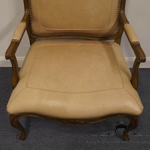 Puede incluir: Un sill&oacute;n de cuero beige con un marco de madera y detalles tallados. El sill&oacute;n tiene un respaldo alto y brazos enrollados.