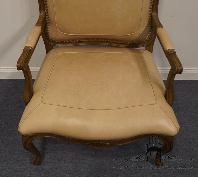 Puede incluir: Un sill&oacute;n de cuero beige con un marco de madera y detalles tallados. El sill&oacute;n tiene un respaldo alto y brazos enrollados.