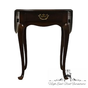 May include: A dark brown, antique drop-leaf table with a single drawer and brass hardware. The table has curved legs and a decorative drawer pull. The table is a classic piece of furniture.