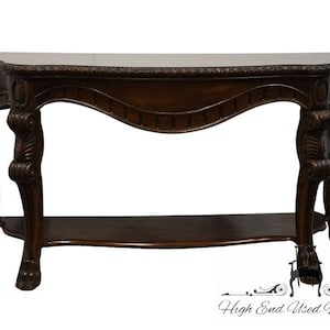 May include: A dark brown wooden console table with ornate carvings and a curved top. The table has a lower shelf and stands on four legs with intricate details.
