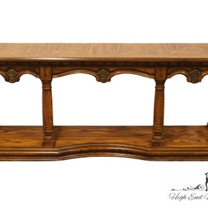 May include: A wooden console table with a warm brown finish. The table features a rectangular top, decorative arched supports, and a lower shelf. The design includes ornate details and brass-colored accents, suitable for a living room or entryway.