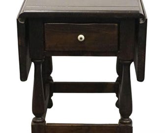 May include: A dark brown, antique drop-leaf side table with a single drawer and a white knob. The table has turned legs and a rectangular top. The table is approximately 24 inches tall.