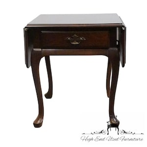 May include: A dark brown, antique side table with a single drawer and a brass handle. The table has a rectangular top with drop leaves and curved legs. The table is made of wood and has a glossy finish.