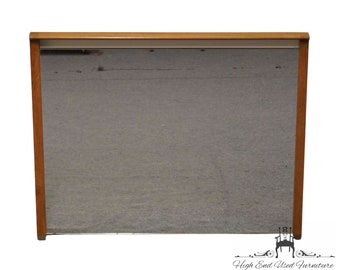 May include: A large rectangular mirror with a wooden frame. The frame is a light brown color and has a simple design. The mirror is reflecting a gray surface.