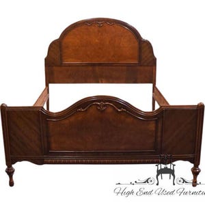 May include: A wooden bed frame featuring a tall, arched headboard and a matching footboard with a curved top edge. The wood displays a rich brown finish with burl wood veneer panels, decorative carved details, and diagonal grain patterns.