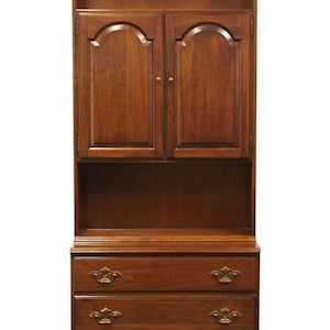 May include: A solid wood bookcase with a curved top and three drawers. The bookcase has two doors with arched panels and brass hardware. The bookcase is a rich brown color.