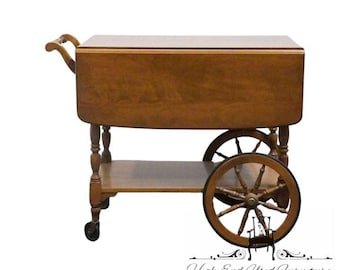 May include: A brown wooden drop-leaf serving cart featuring a rectangular top with two hinged side leaves, a lower shelf, and four legs. The cart is supported by two large spoked wheels on one side and two smaller casters on the other side.