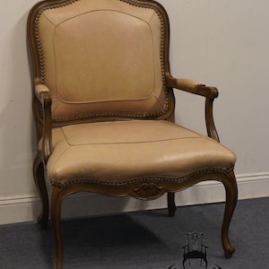 Puede incluir: Un sill&oacute;n de cuero beige con un marco de madera tallada. El sill&oacute;n tiene un respaldo alto y brazos enrollados. El sill&oacute;n est&aacute; tapizado en cuero beige claro.