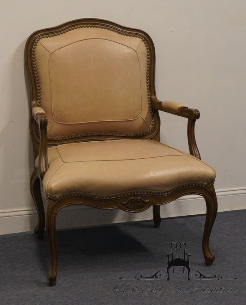 Puede incluir: Un sill&oacute;n de cuero beige con un marco de madera tallada. El sill&oacute;n tiene un respaldo alto y brazos enrollados. El sill&oacute;n est&aacute; tapizado en cuero beige claro.