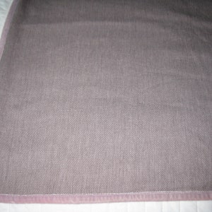 May include: A close-up of a light brown fabric with a subtle texture. The fabric has a pink border around the edges.
