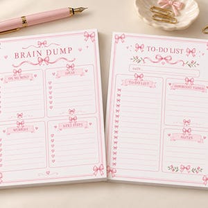 May include: Two rectangular paper notepads with pink bow and heart illustrations. The left pad is titled BRAIN DUMP with sections for ON MY MIND, IDEAS, WORRIES, and NEXT STEPS. The right pad is titled TO-DO LIST with sections for TO-DO LIST, IMPORTANT THINGS, and NOTES.