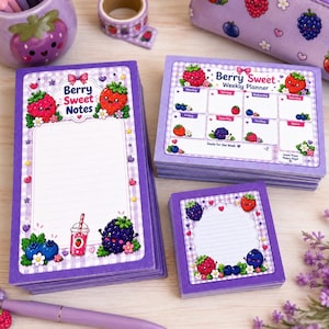May include: A set of purple stationery featuring berry-themed designs, including a tall notepad labeled Berry Sweet Notes, a weekly planner, and a square sticky note pad, all decorated with cartoon strawberries, blueberries, and blackberries.