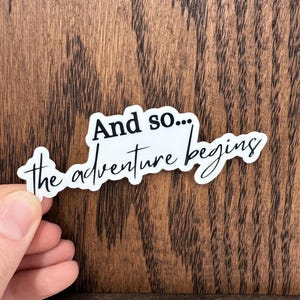 May include: White sticker with black text that reads "And so... the adventure begins".