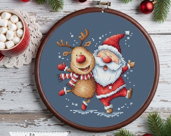 Könnte beinhalten: Ein Kreuzstich-Stickrahmen mit dem Weihnachtsmann und einem Rentier, die tanzen. Beide Figuren tragen rot-weiße Outfits vor blauem Hintergrund. Der Holzrahmen ist von Weihnachtsdekorationen umgeben, darunter Kugeln und Tannenzweige.