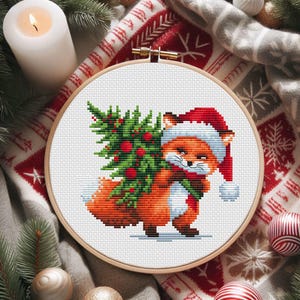 Può includere: Ricamo a punto croce in un telaio di legno raffigurante una volpe con cappello e sciarpa da Babbo Natale, che trasporta un albero di Natale. La volpe è arancione e bianca, l'albero è verde con bacche rosse. Decorazioni festive.