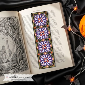 Può includere: Un segnalibro fatto a mano con un motivo geometrico viola, bianco, arancione e nero. Il segnalibro è posto in un libro aperto con illustrazioni. Il segnalibro ha il testo "natalka stitch studio" e "NatalkaStudio.etsy.com".