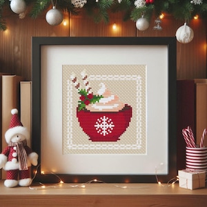 Peut inclure: Modèle de point de croix d'une tasse rouge avec de la crème fouettée, des cannes en sucre et du houx. La tasse a un motif de flocon de neige et est encadrée d'un cadre blanc.